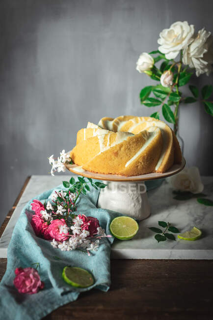 Tasty lime sponge cake served on white plate near flowers and lime slices — Stock Photo
