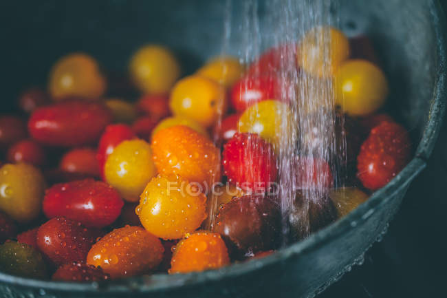 Cherry tomatoes in a colander under running water — Stock Photo